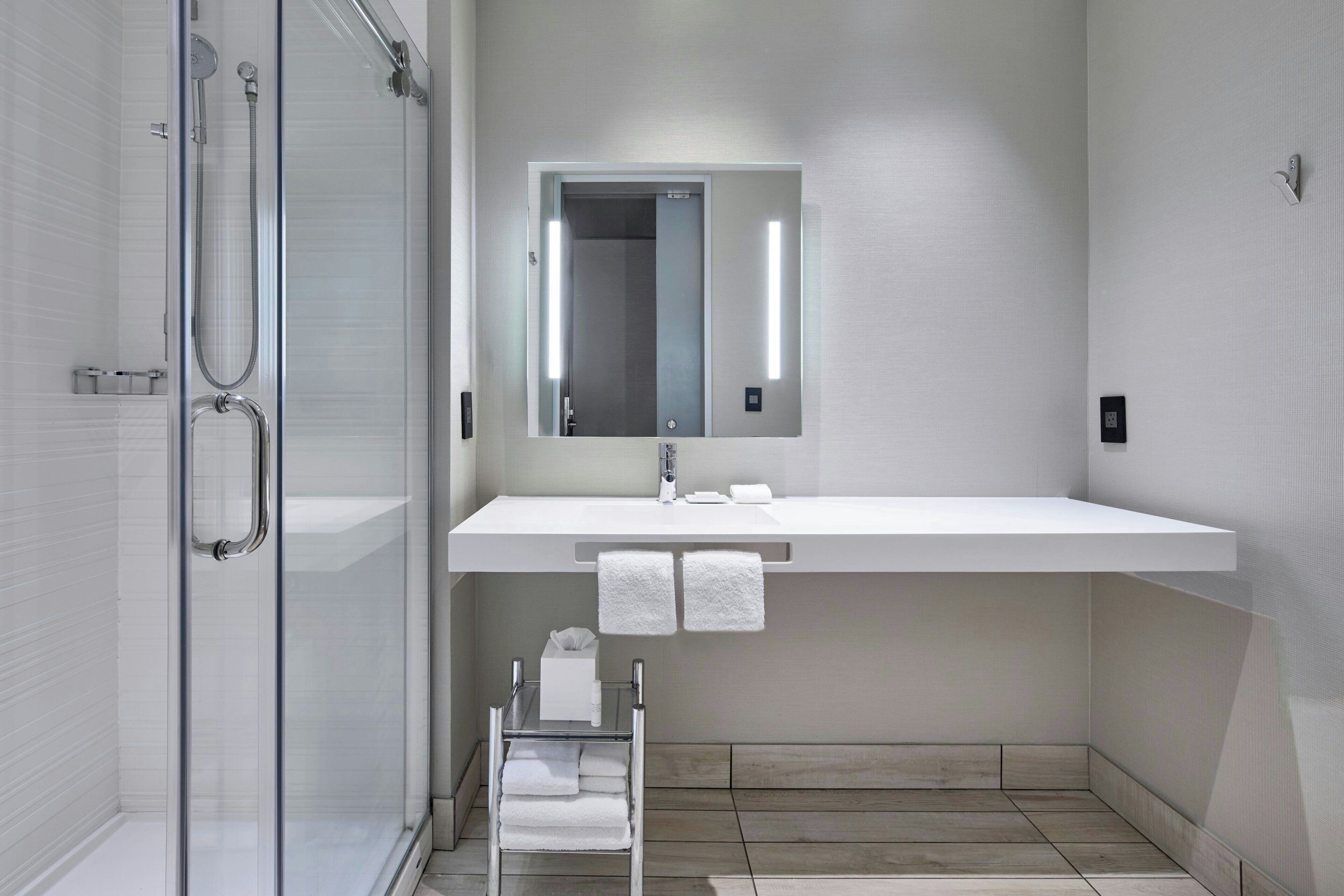 Un baño moderno con cabina de ducha de vidrio, un lavamanos blanco con espejo encima y un perchero con toallas dobladas.