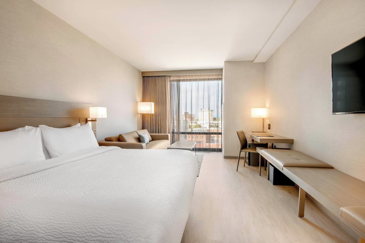 Une chambre d’hôtel moderne, dotée d’un grand lit, d’un bureau, d’une chaise et d’un téléviseur fixé au mur.