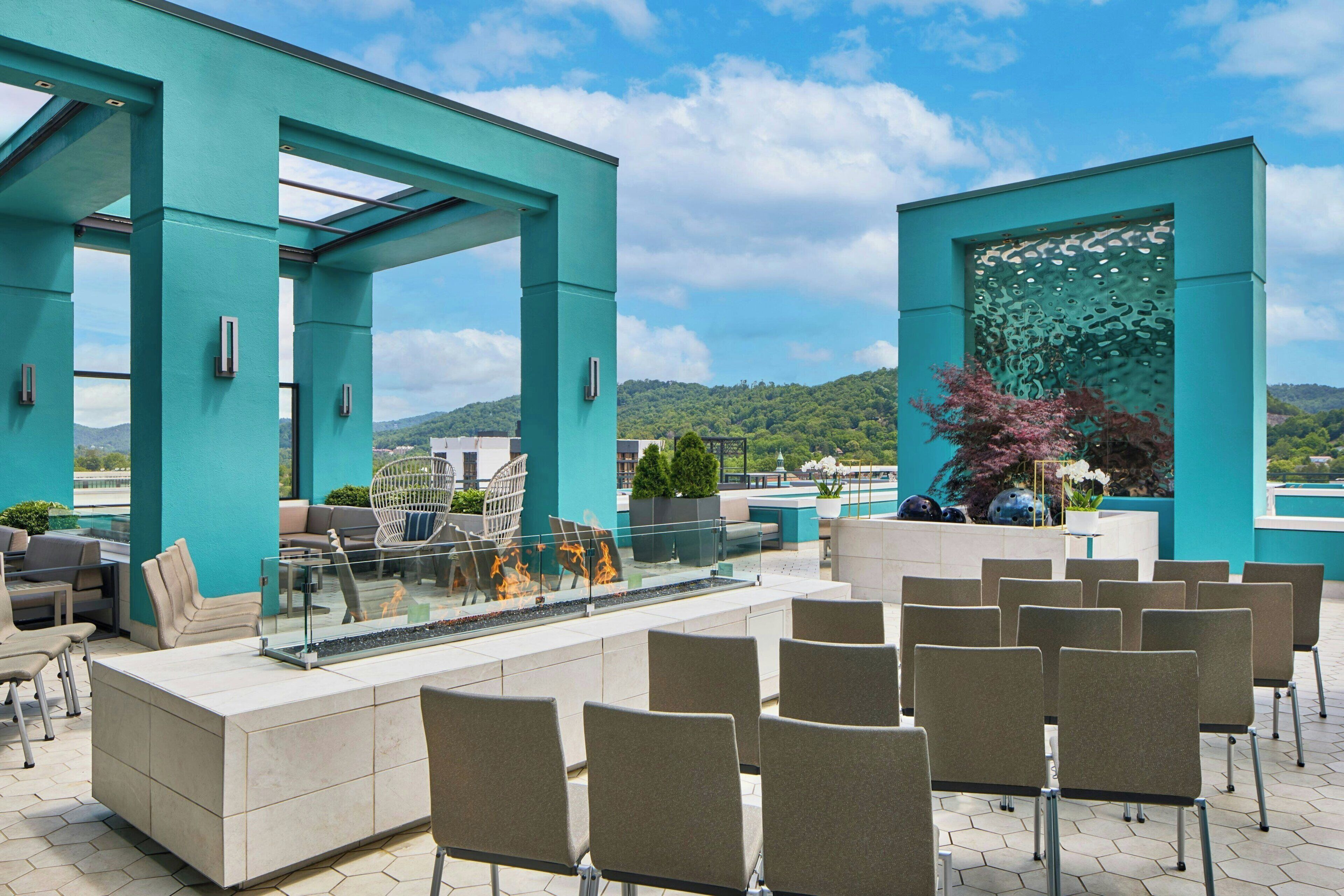 Eine Dachterrasse mit Sitzgelegenheiten, einem Feuerelement und Blick auf die umliegende Landschaft.
