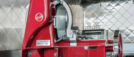 A red Berkel meat slicer in a kitchen with a diamond-patterned backsplash.