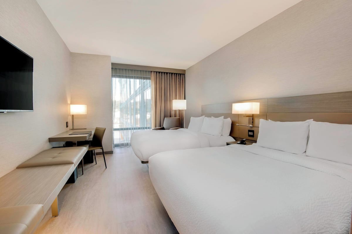 Une chambre d’hôtel avec deux lits, un bureau, une chaise, une télévision et une fenêtre avec des rideaux.