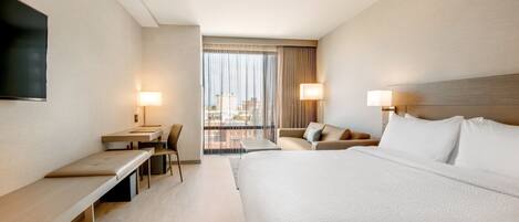 Una habitación de hotel con una cama grande, un escritorio, una silla y un televisor montado en la pared.