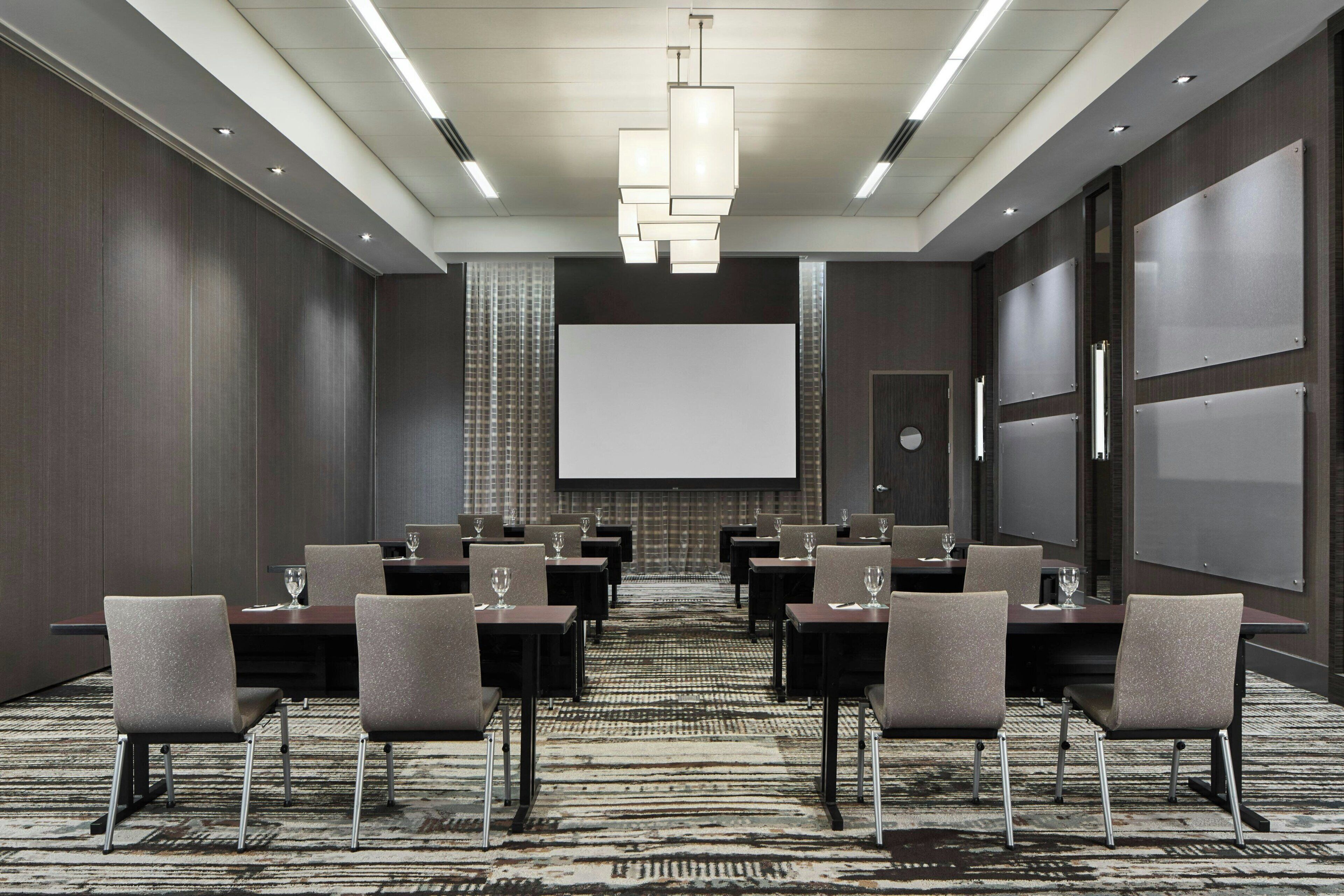 Un salón de conferencias con una pantalla grande, varias mesas y sillas.