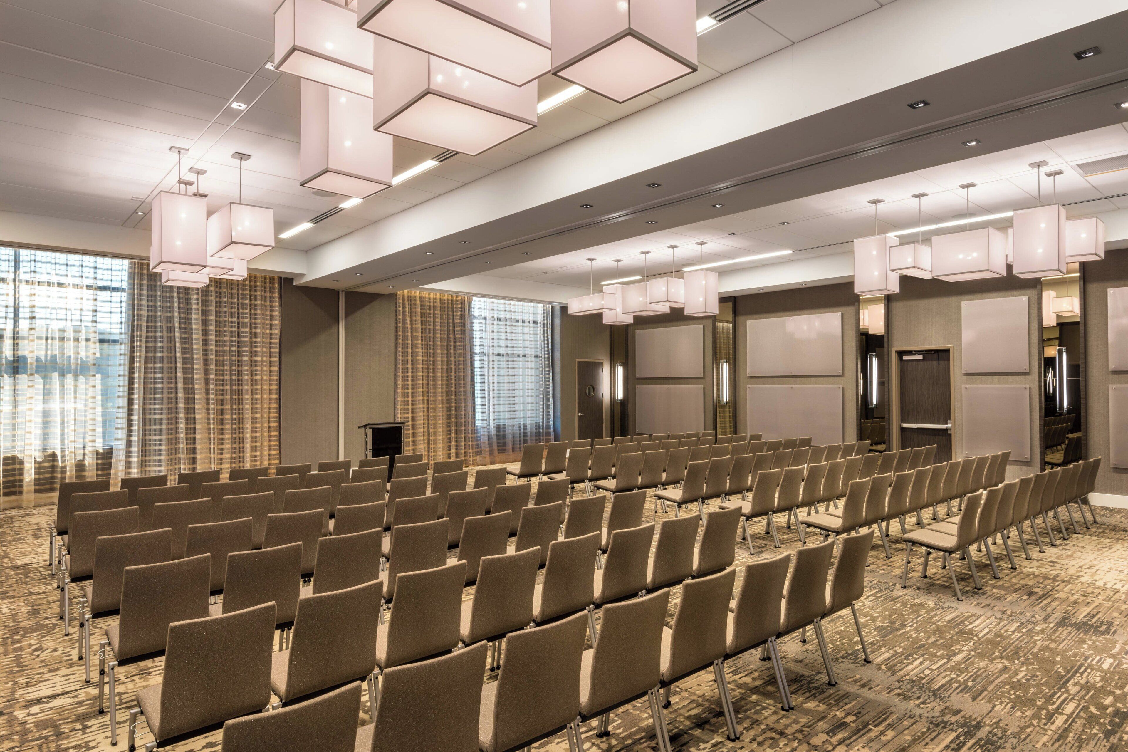 Un salón de conferencias con hileras de sillas, piso alfombrado e iluminación colgante moderna.
