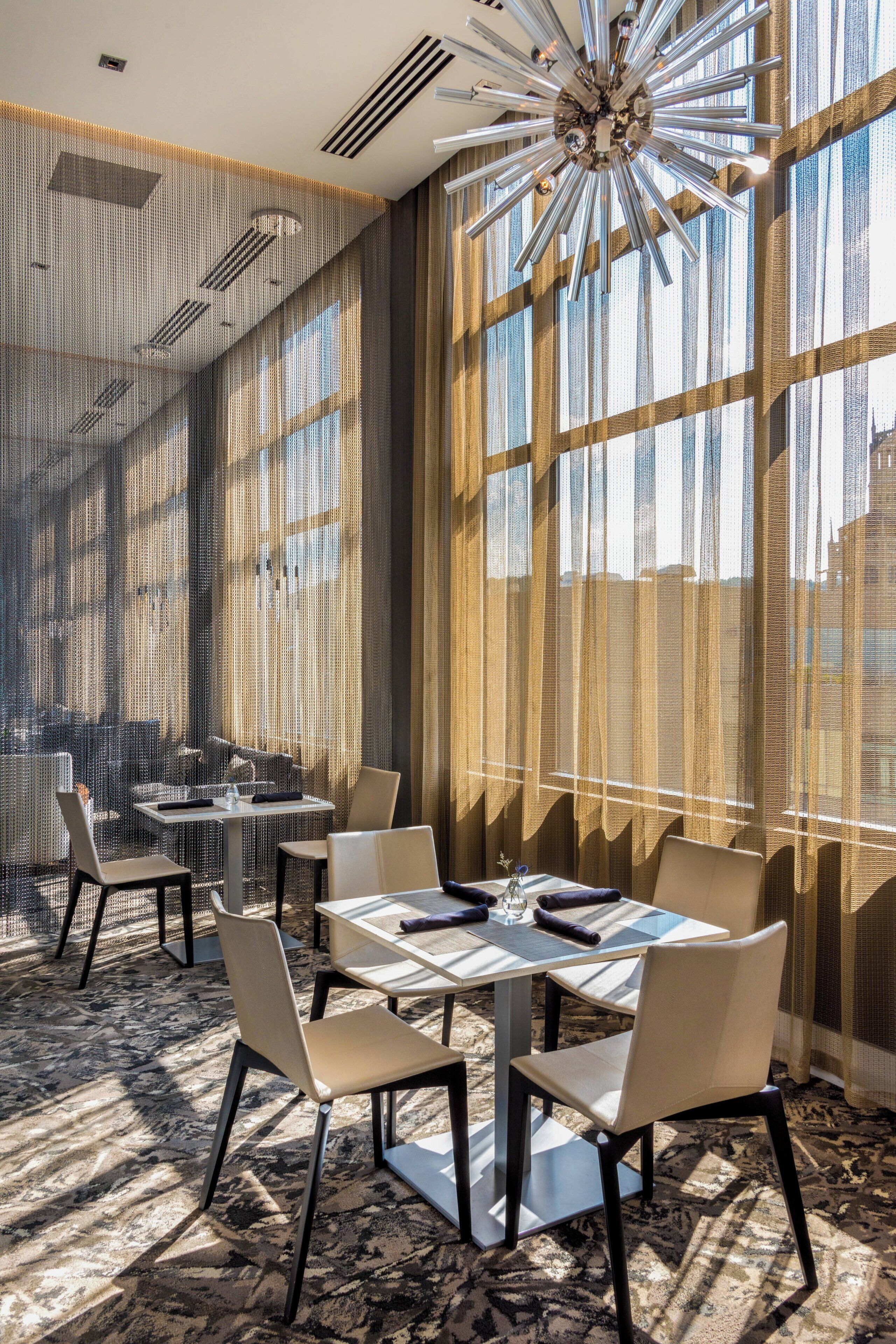 Een moderne hotelkamer met grote ramen, een kroonluchter en een kamerbreed tapijt.