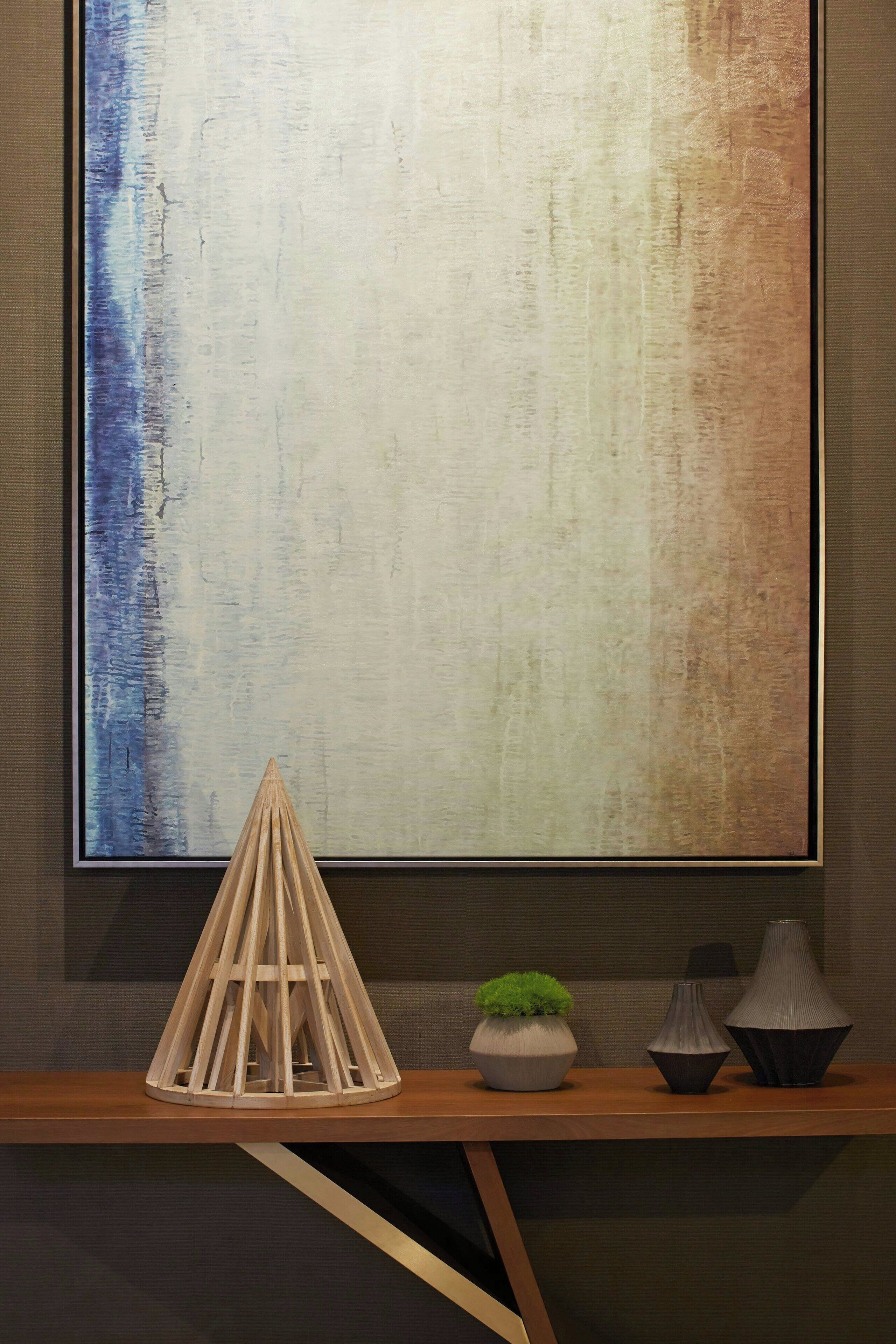 Een modern interieur met een houten tafel waarop drie vazen en een geometrisch sculptuur staan.