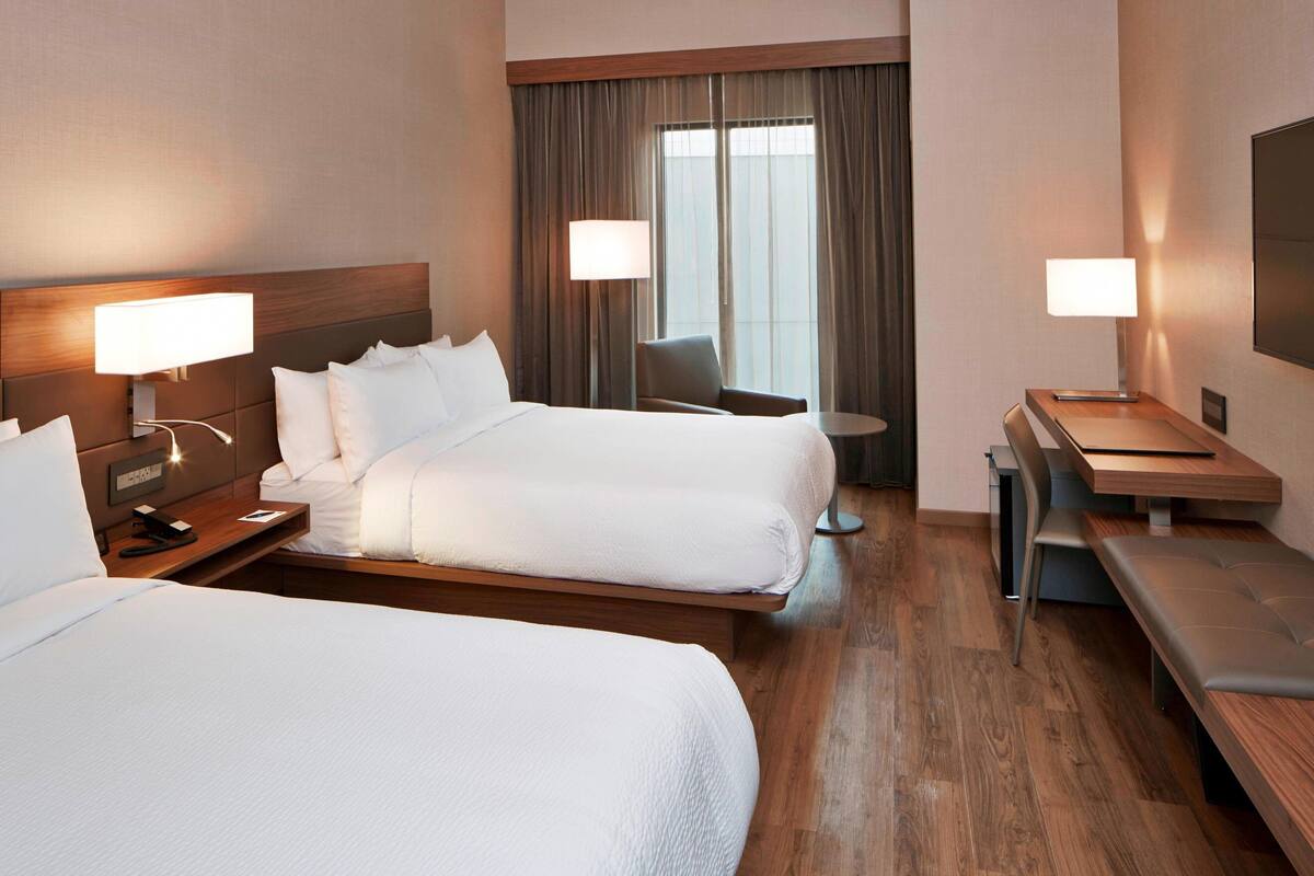 Una habitación de hotel con dos camas, un escritorio, una silla y una mesita.