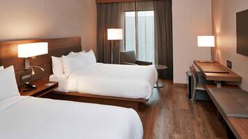 A hotel room with two beds, a desk, a chair, and a small table.