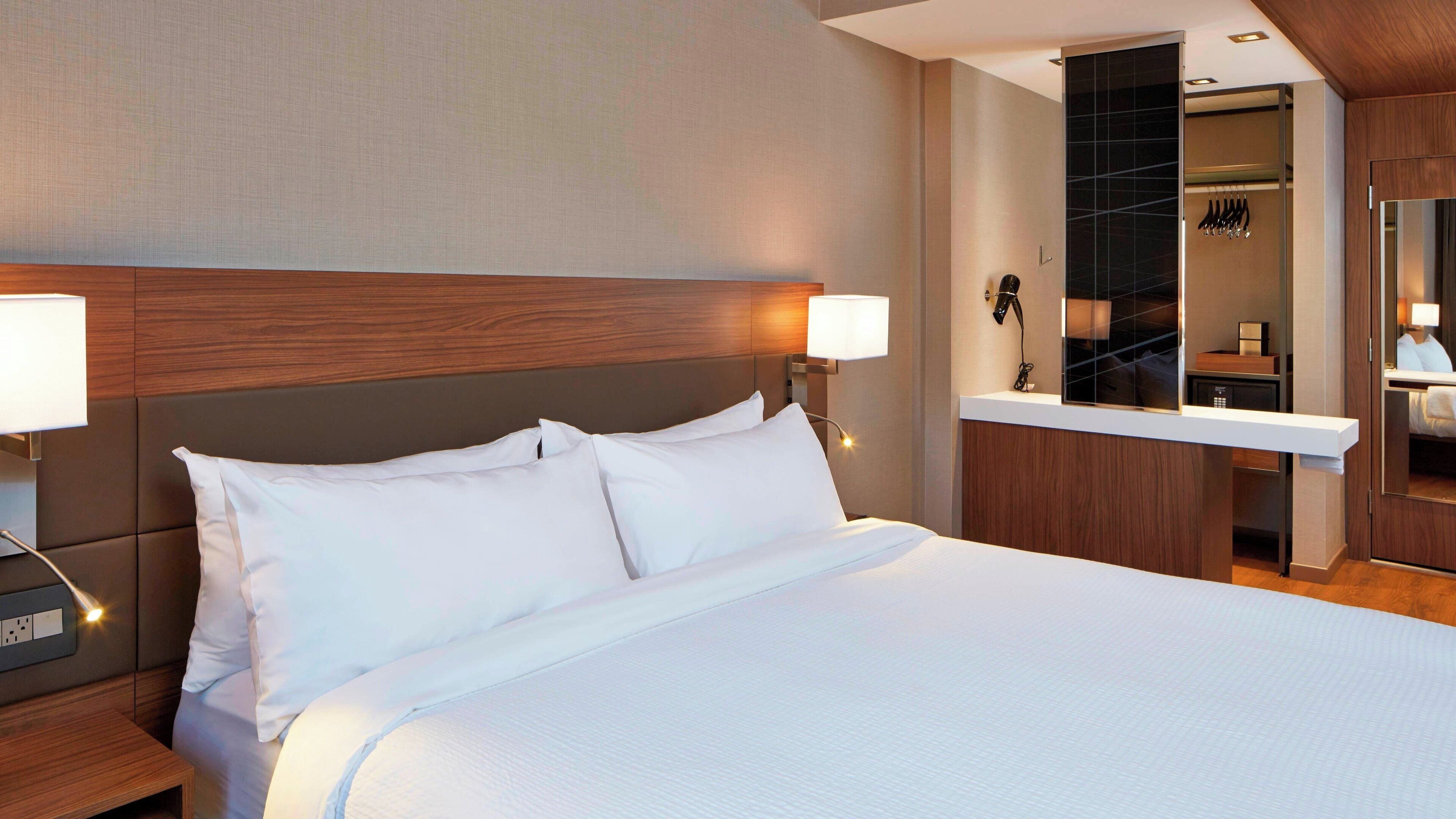 Une chambre d’hôtel avec un grand lit, des lampes de chevet, une tête de lit en bois, un bureau intégré et un miroir.