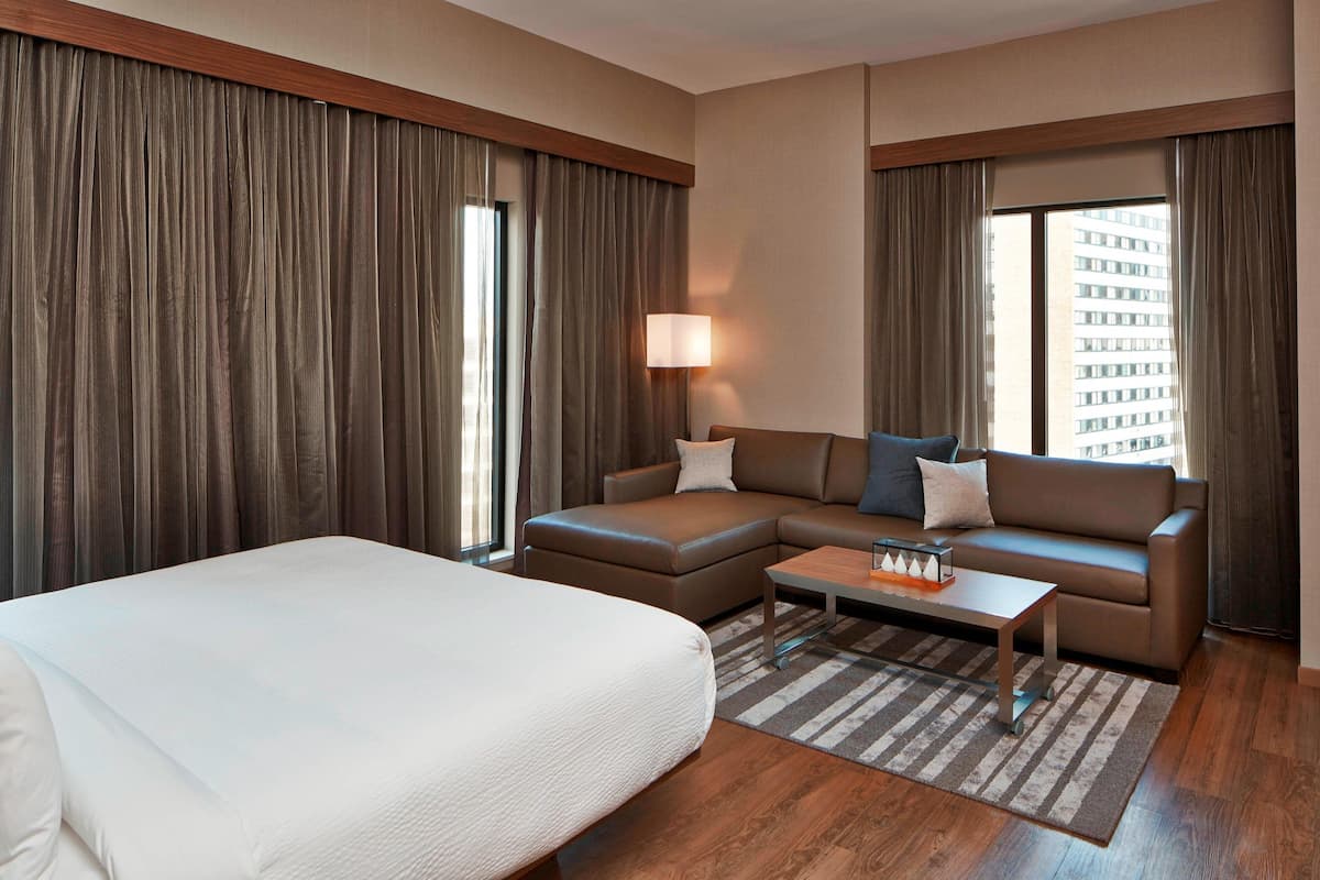 Una habitación de hotel con una cama grande, un sofá, una mesa de centro y una lámpara.