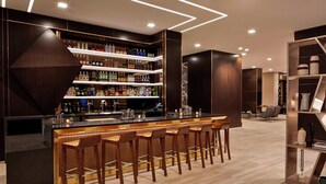 A modern bar area with multiple shelves of liquor bottles, a long bar counter, and several bar stools.