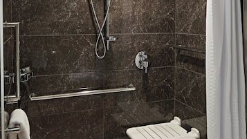 A modern shower area with a glass door, a handheld showerhead, a wall-mounted faucet, and a white shower seat.
