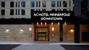 The exterior of AC Hotel Minneapolis Downtown, featuring a stone facade, large entrance, and string lights.