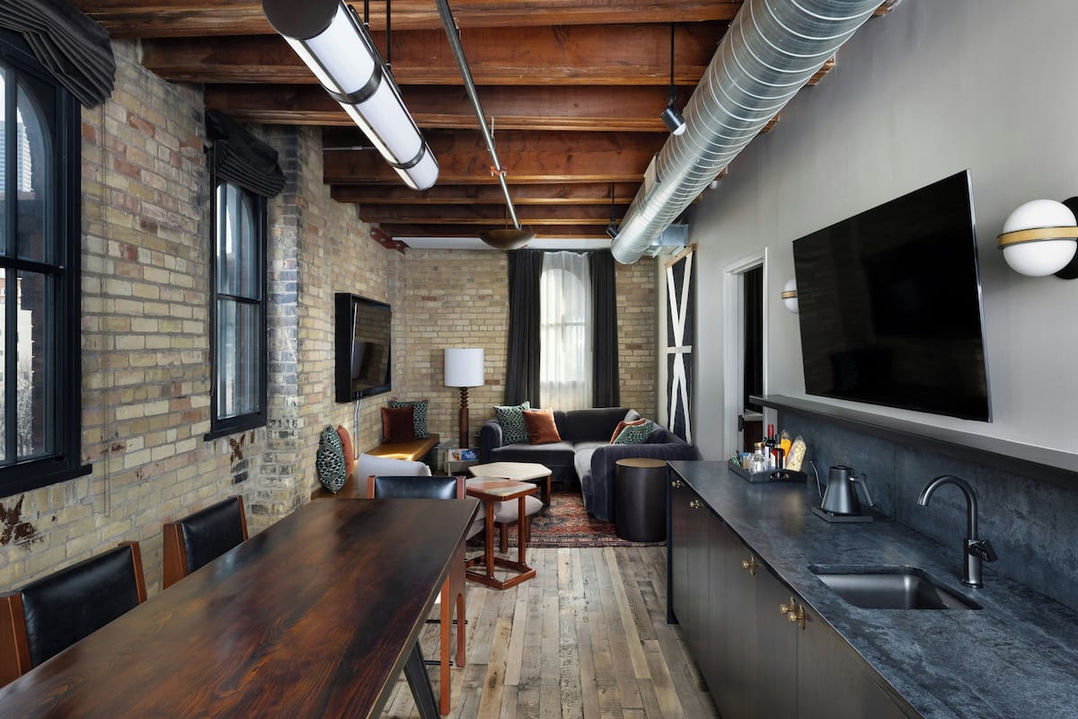 A modern kitchen with a large TV, a dining area with a long wooden table, and a cozy seating area with a sofa and chairs.