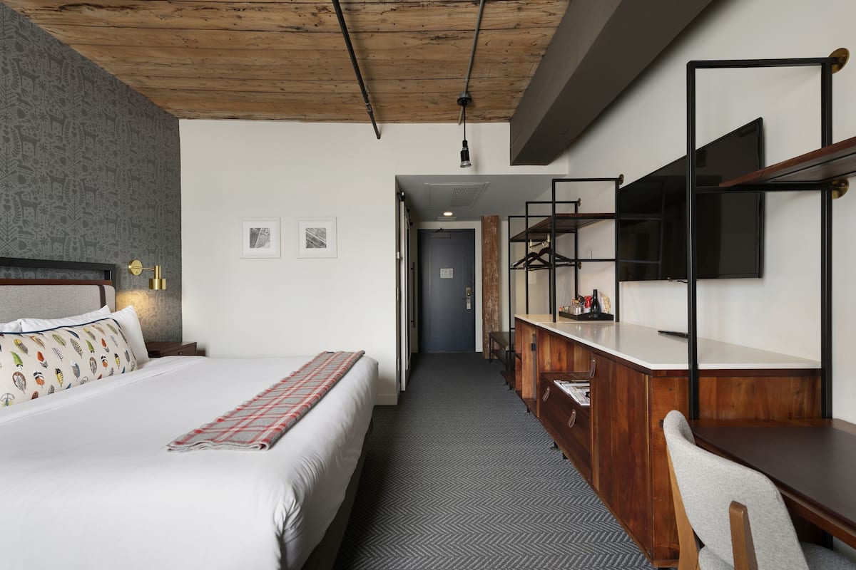 A hotel room with a bed, a desk with a mirror, a wardrobe, and a door leading to another room.
