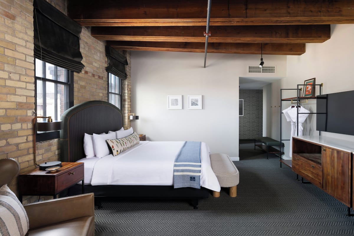A hotel room with a bed, a wooden bench, a desk, a TV, and a wardrobe.