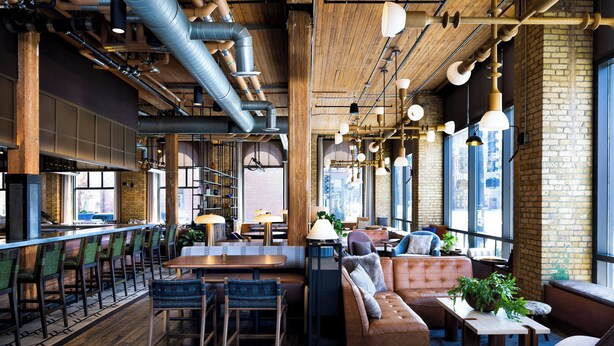 Un restaurante con suelos de madera, una zona de bar y un área de estar con sofá y sillas.