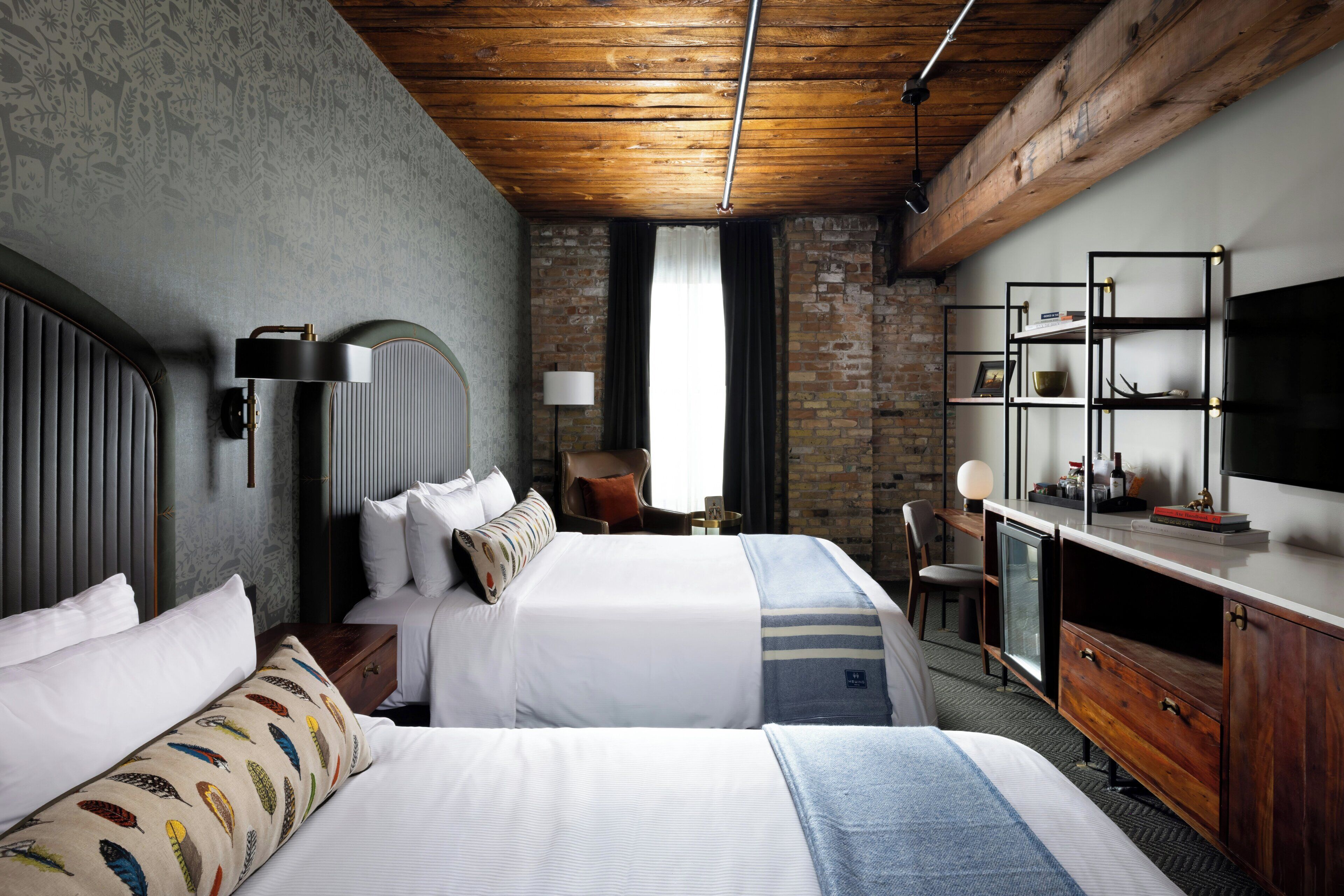 Habitación de hotel con dos camas, un escritorio, un televisor y una pared de ladrillo.