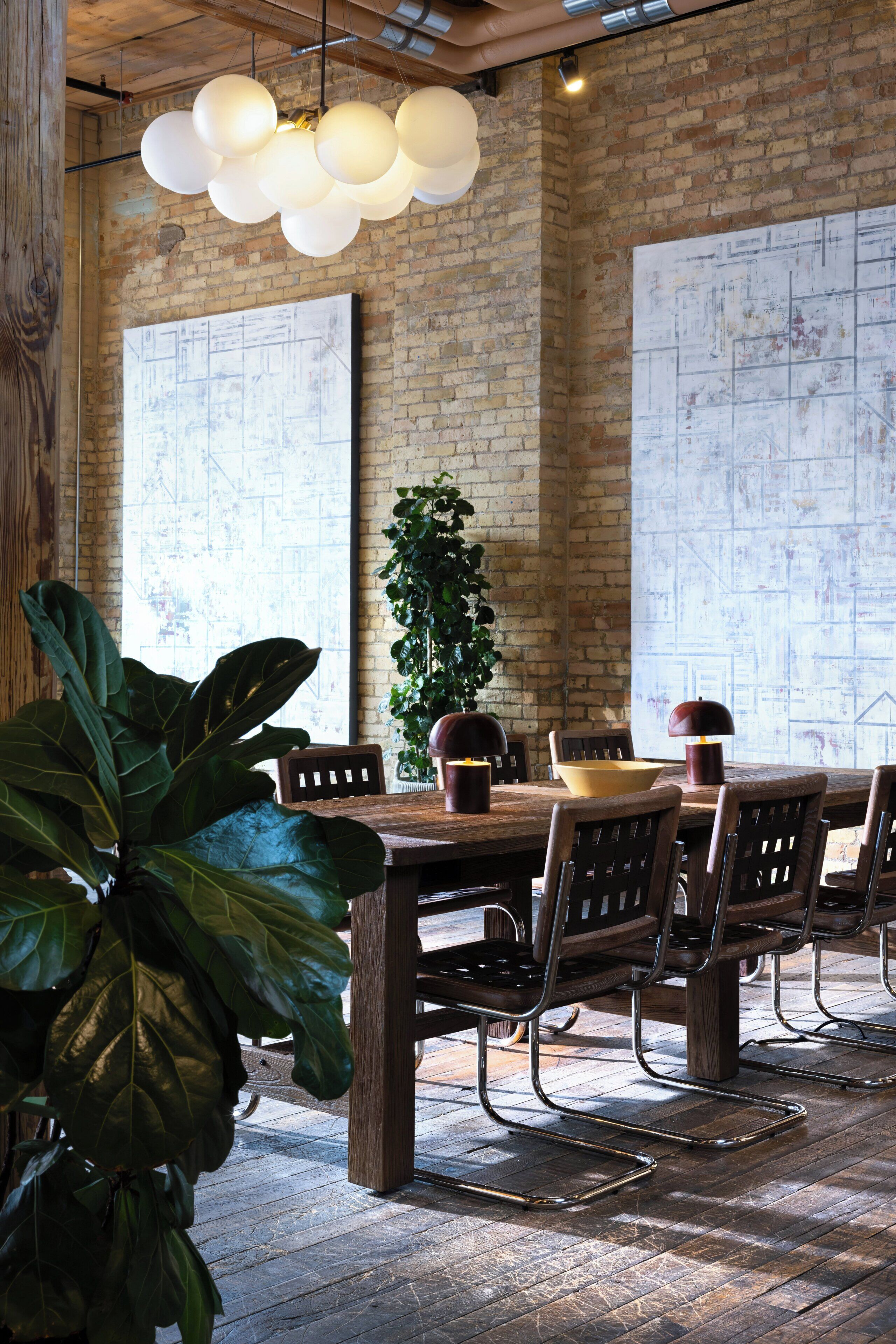 A rustic dining area with exposed brick walls, a wooden table, metal chairs, and hanging spherical light fixtures.