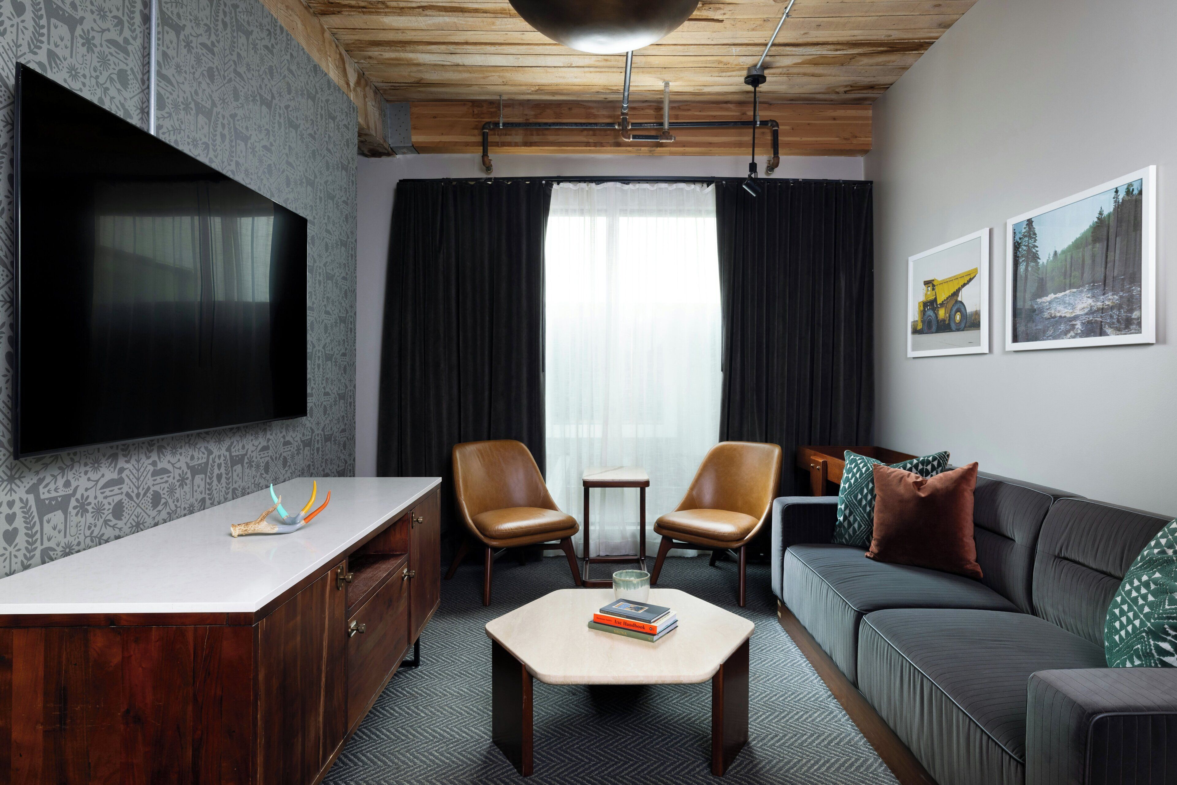 A modern living room with a flat-screen TV, leather armchairs, a sofa, a coffee table, and artwork on the walls.