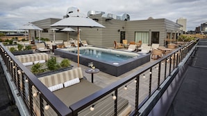 Un área de piscina en la azotea con sillones, sombrillas y un jacuzzi.