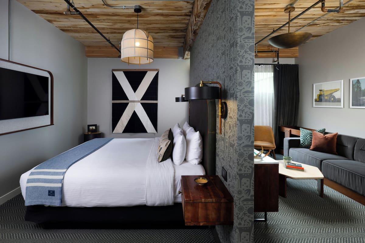 A hotel room with a bed, bedside table, lamp, and a sofa.