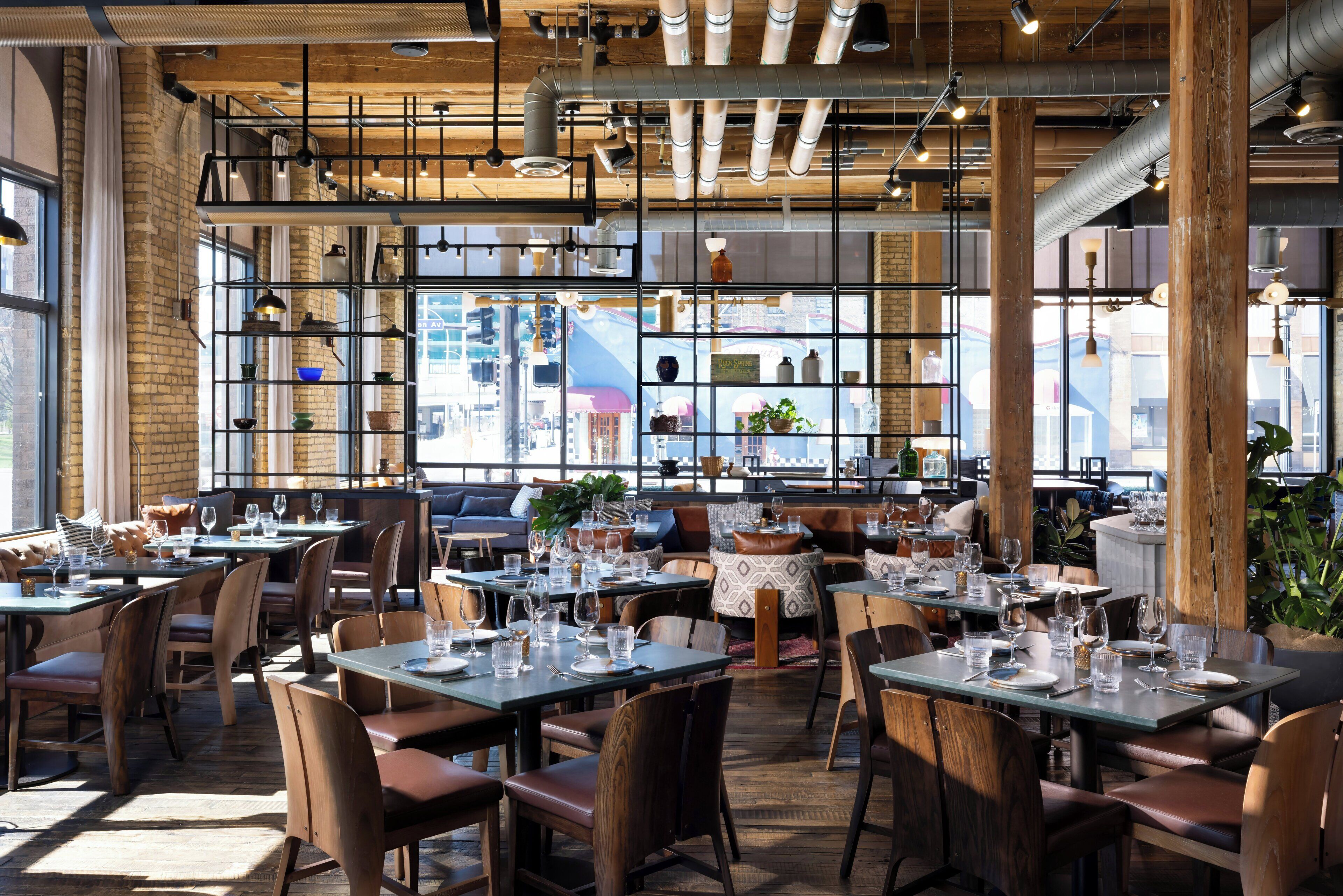 Ein Restaurant mit gedeckten Tischen, Holzbalkendecke und großen Fenstern mit Blick auf die Stadt.