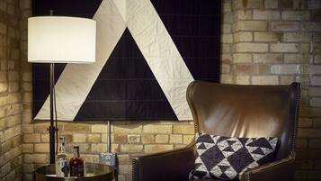 A leather armchair with a patterned pillow, a table with bottles and glasses, and a large wall tapestry.