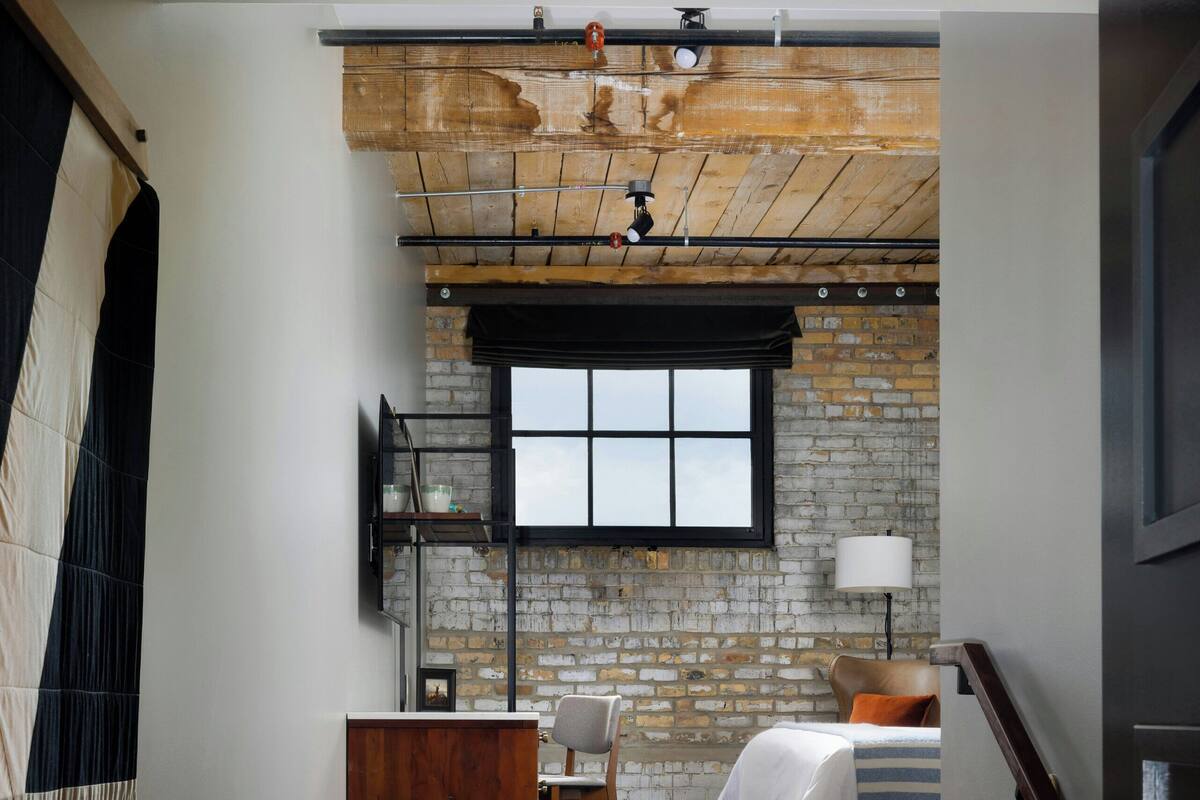 A bedroom with a brick wall, a bed, a desk, and a chair.