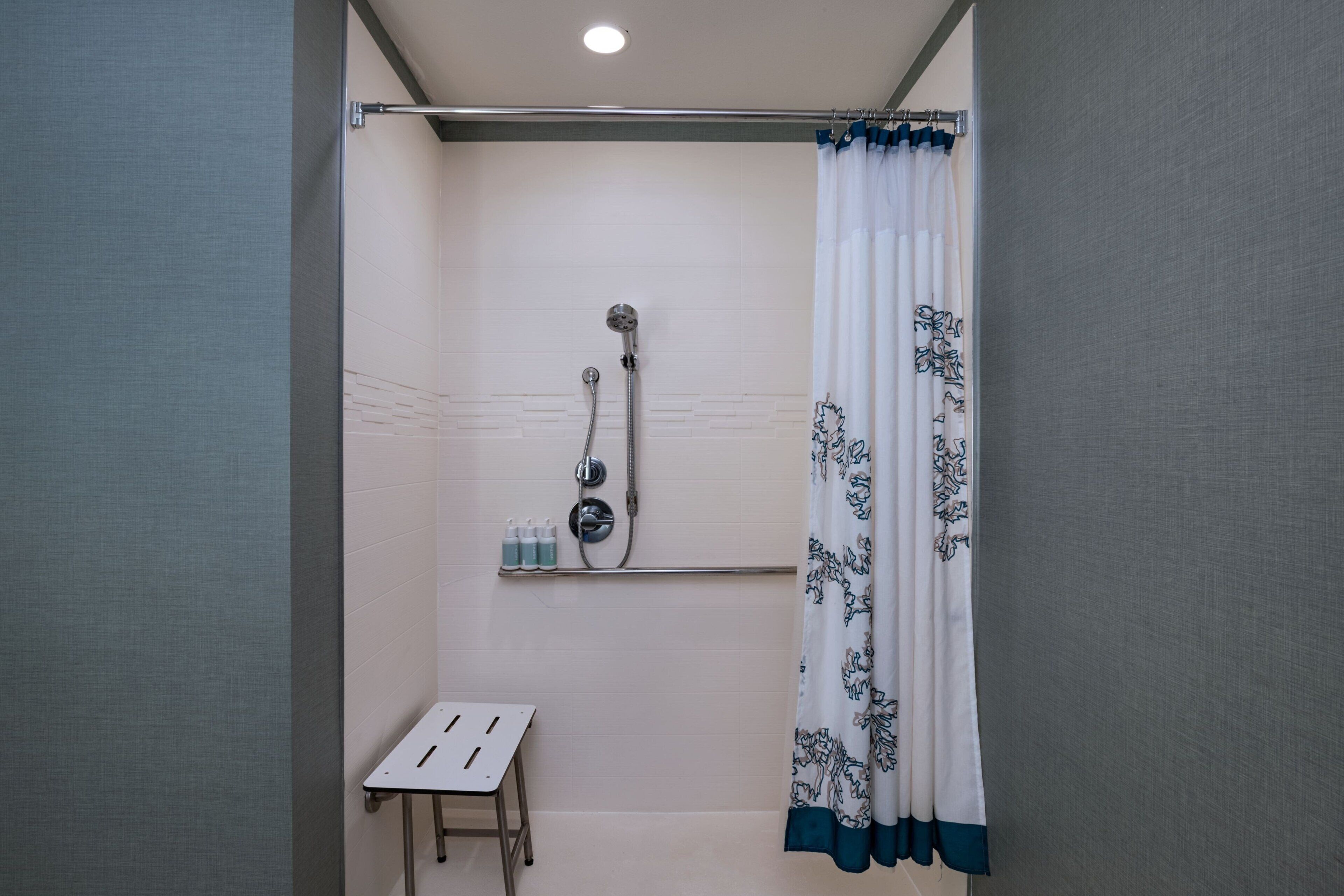 Un espace douche équipé d’un pommeau de douche, d’une étagère avec des bouteilles et d’une petite table.