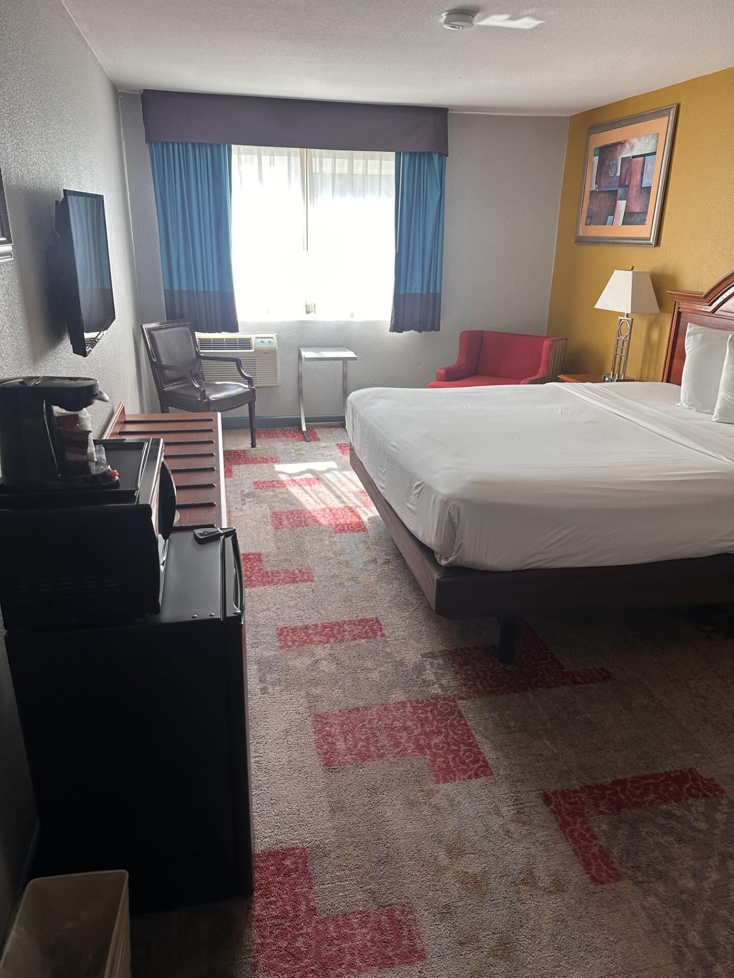 A hotel room with a bed, a desk, a chair, a TV, and a coffee machine.