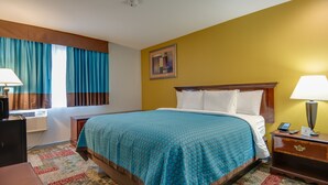 A hotel room with a bed, a nightstand with a lamp, a desk with a lamp, and a window with curtains. - Americas Best Value Inn Hayward (Hayward)