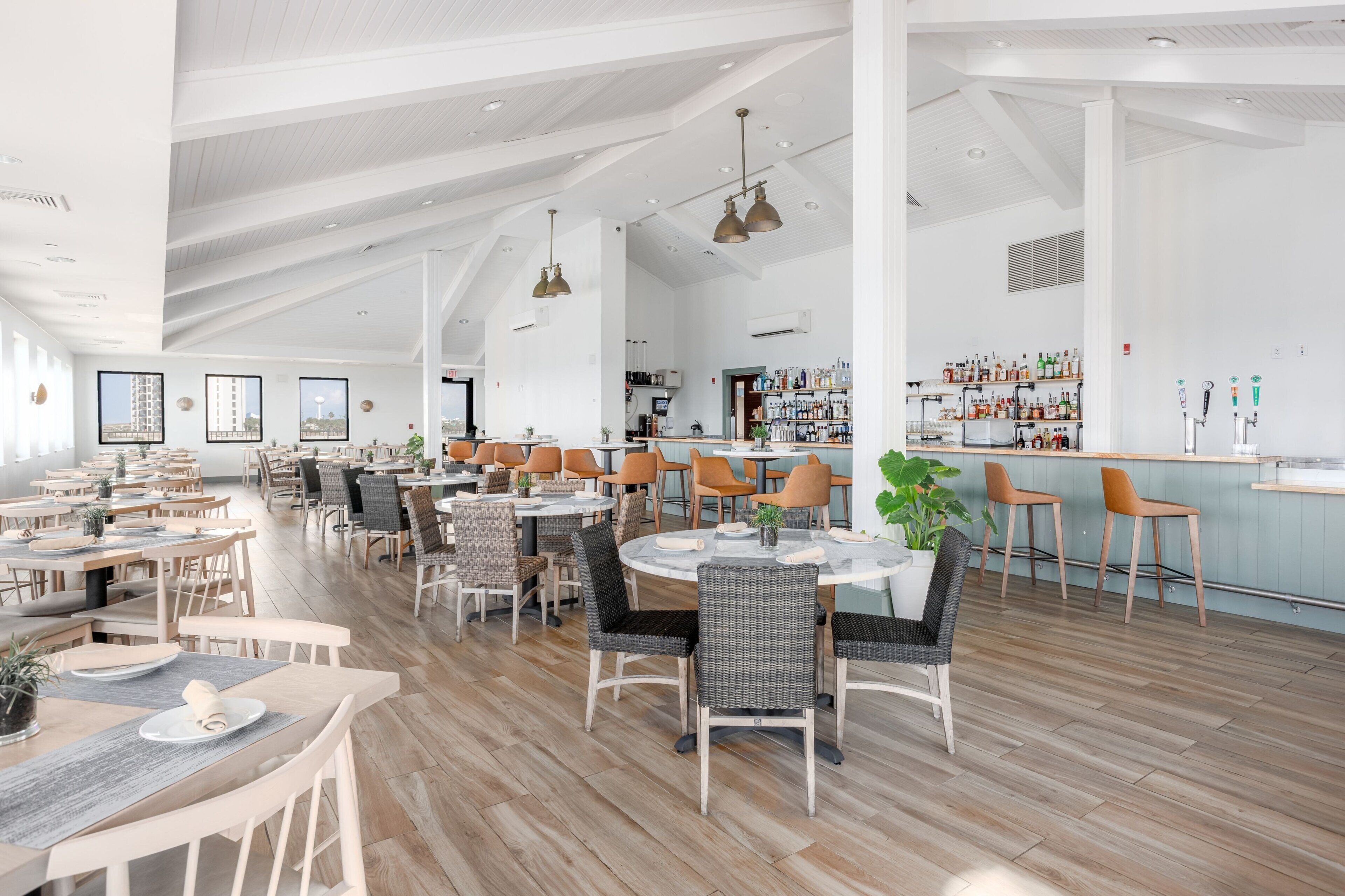 A spacious restaurant with high ceilings, wooden floors, and a variety of seating options including round tables and bar stools.