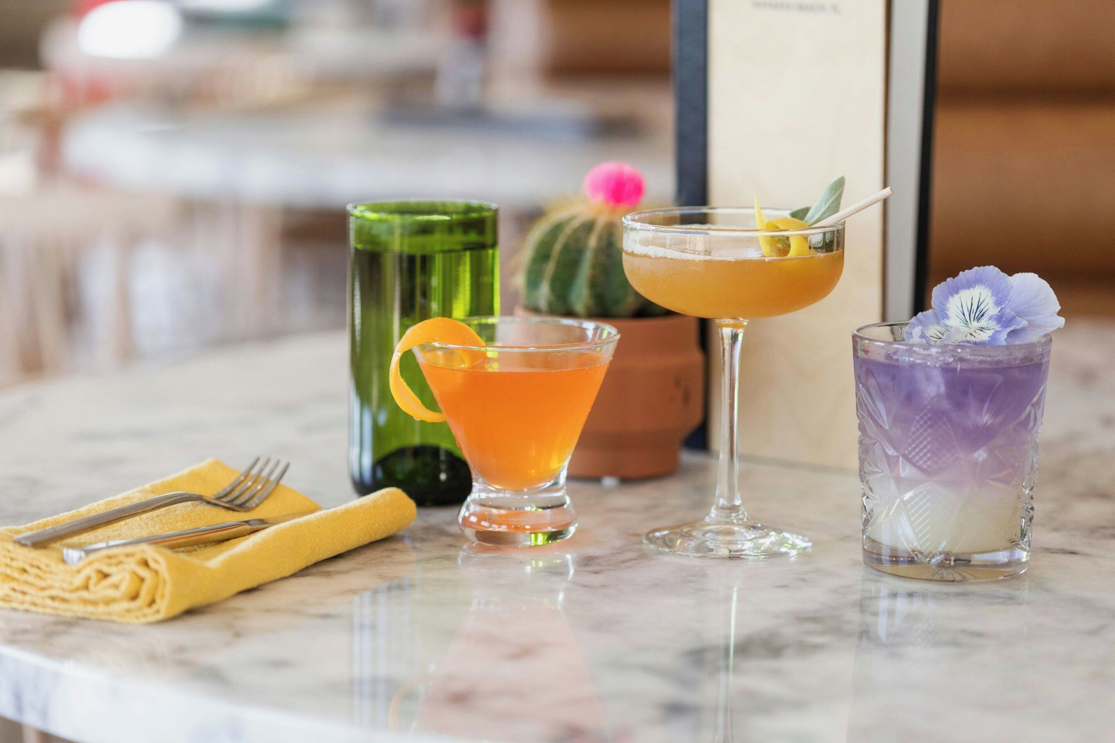Zona de bar con tres cócteles, un vaso verde y una planta de cactus.