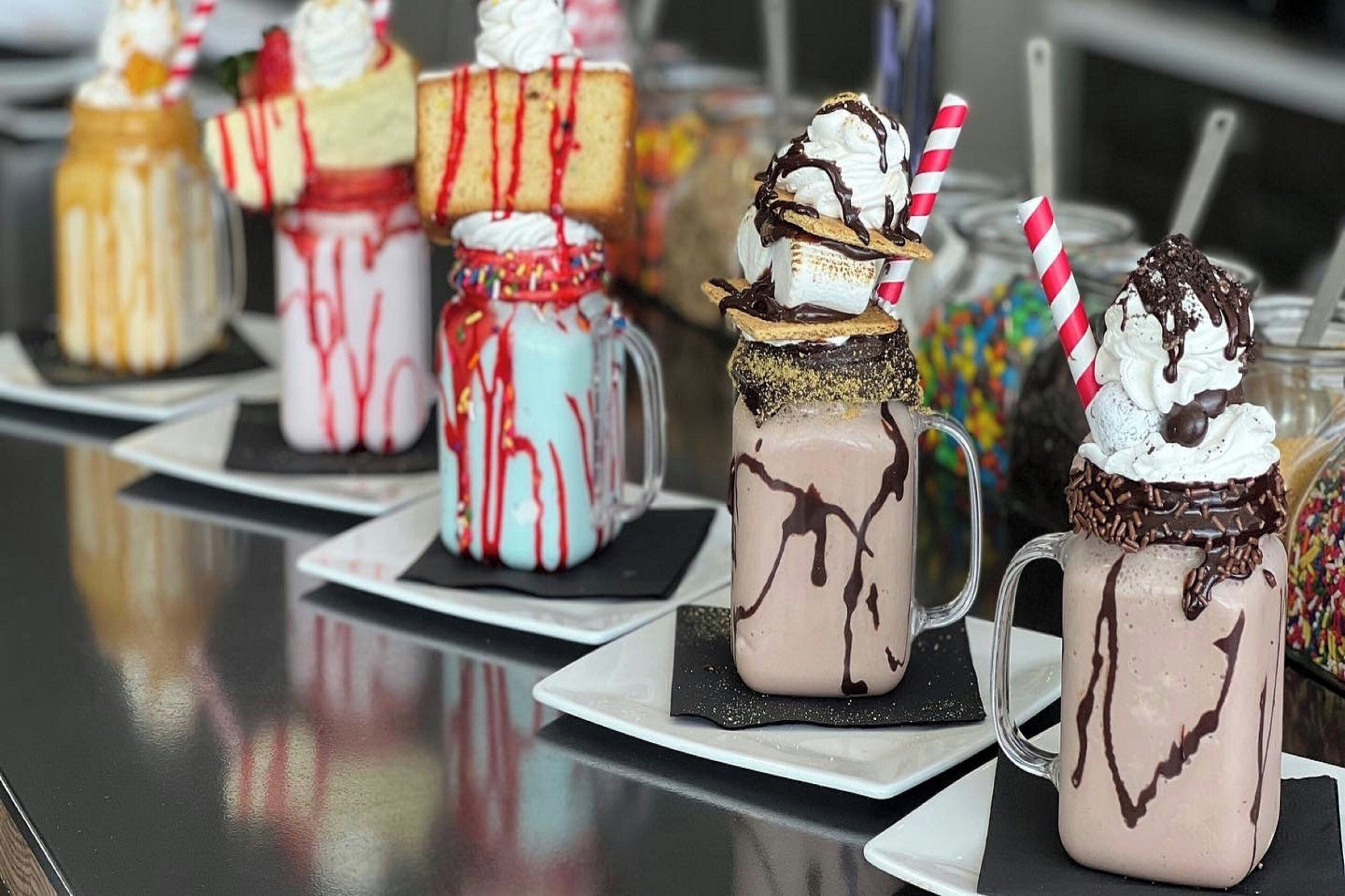 Une variété de boissons dessert servies dans des pots Mason, chacune surmontée de crème fouettée et nappée de sauce au chocolat.