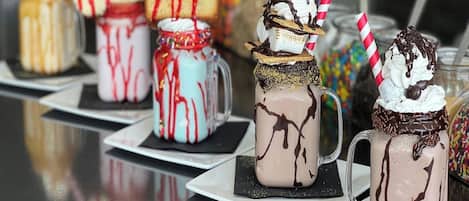 Une variété de boissons dessert servies dans des pots Mason, chacune surmontée de crème fouettée et nappée de sauce au chocolat.