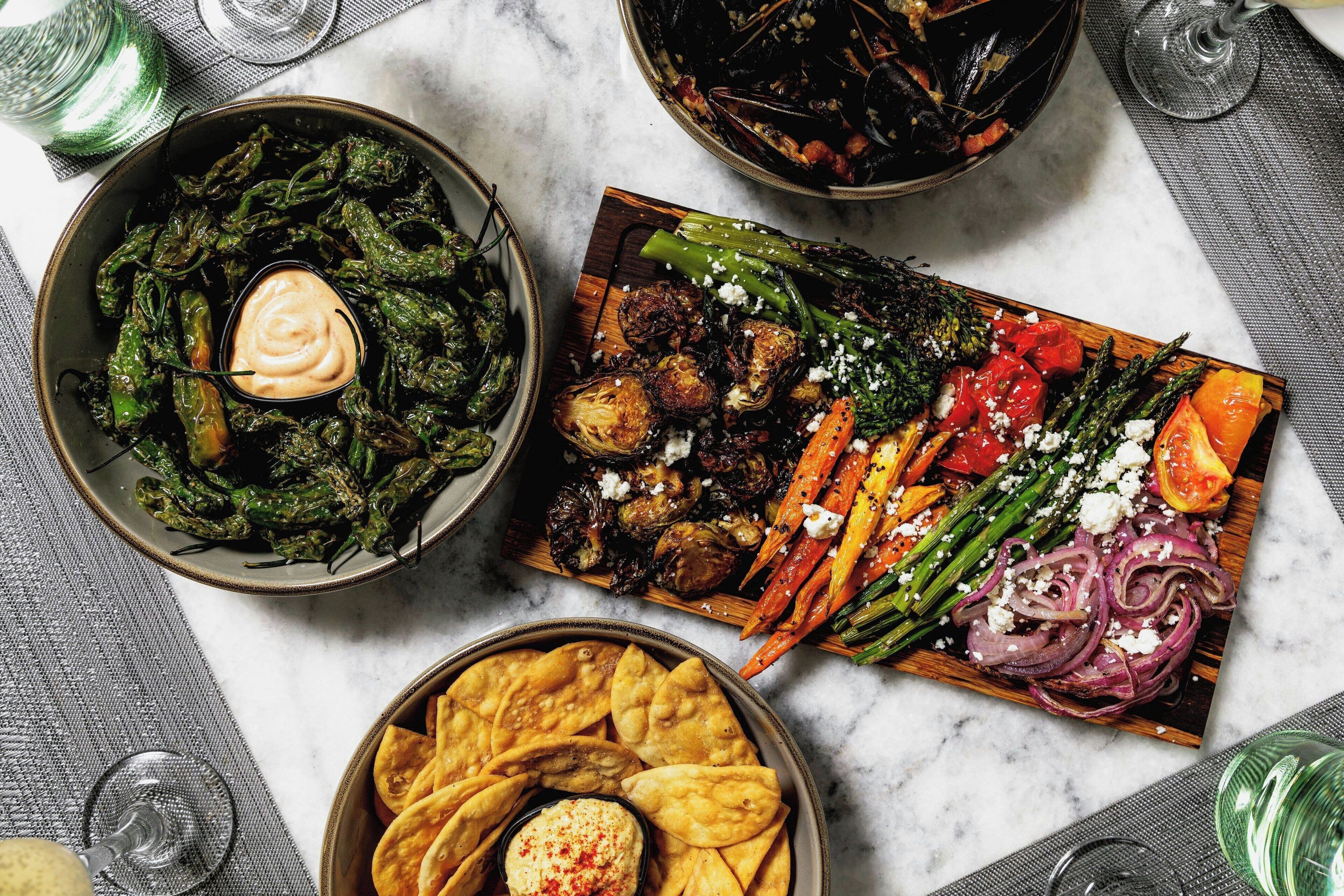 A variety of dishes including roasted vegetables, a bowl of greens, and pita chips with dip.
