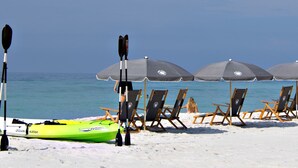A beach with rows of beach chairs and umbrellas, kayaks, and paddleboards.