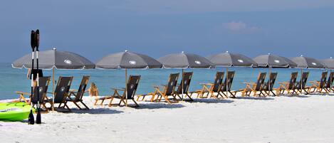 A beach with rows of beach chairs and umbrellas, kayaks, and paddleboards.
