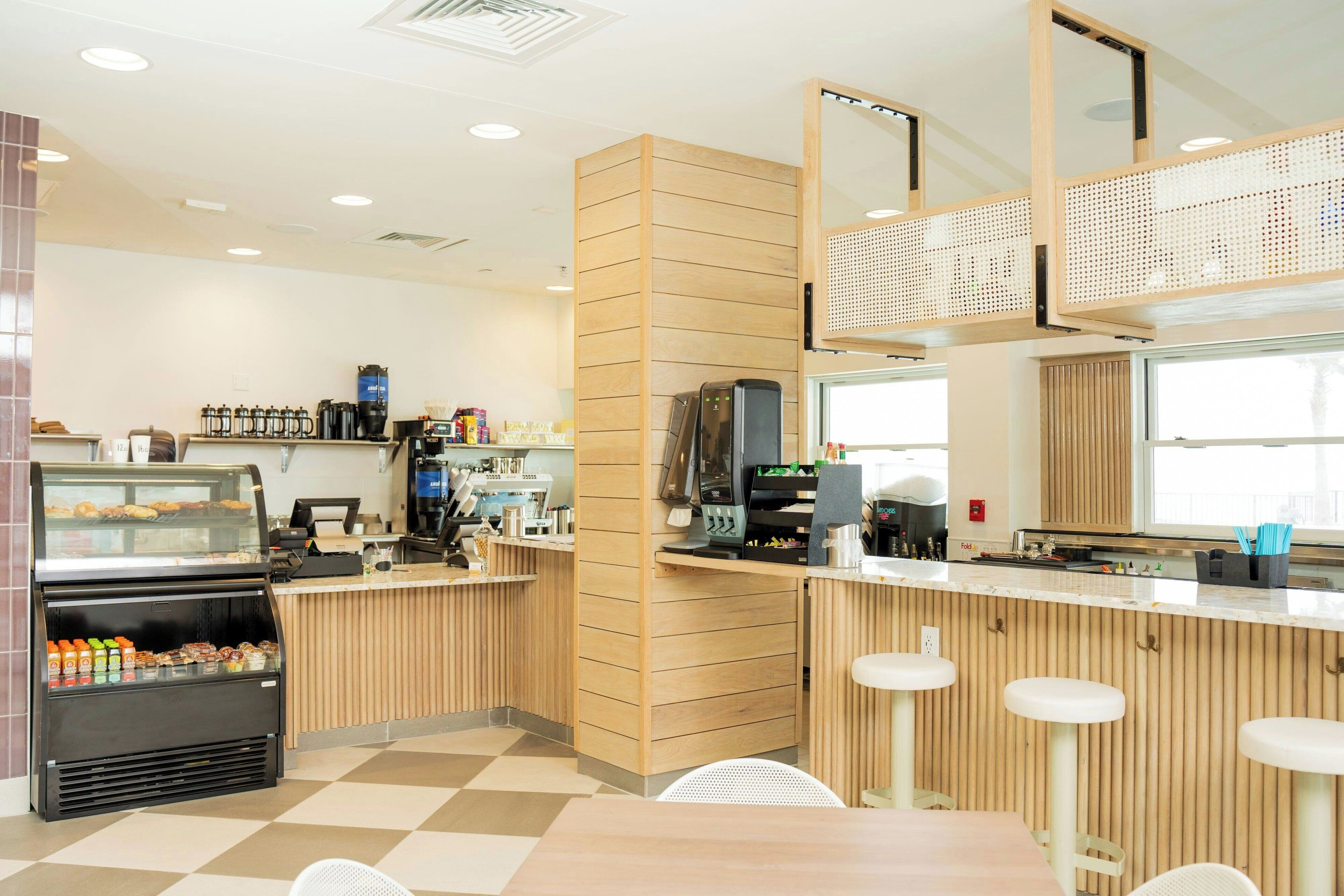 Ett modernt kafé med en bardisk, sittplatser och ett vitrinskåp med bakverk.