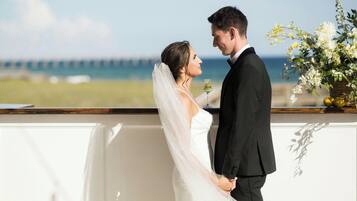 A couple holding hands at a seaside venue with a view of the ocean and a pier in the background.