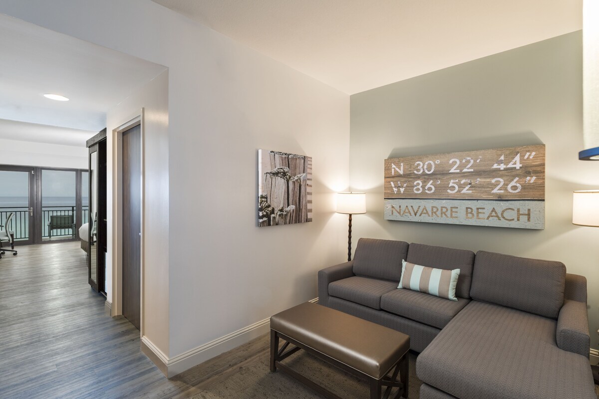 A modern living room with a gray sofa, a bench, and a wall-mounted sign displaying coordinates.