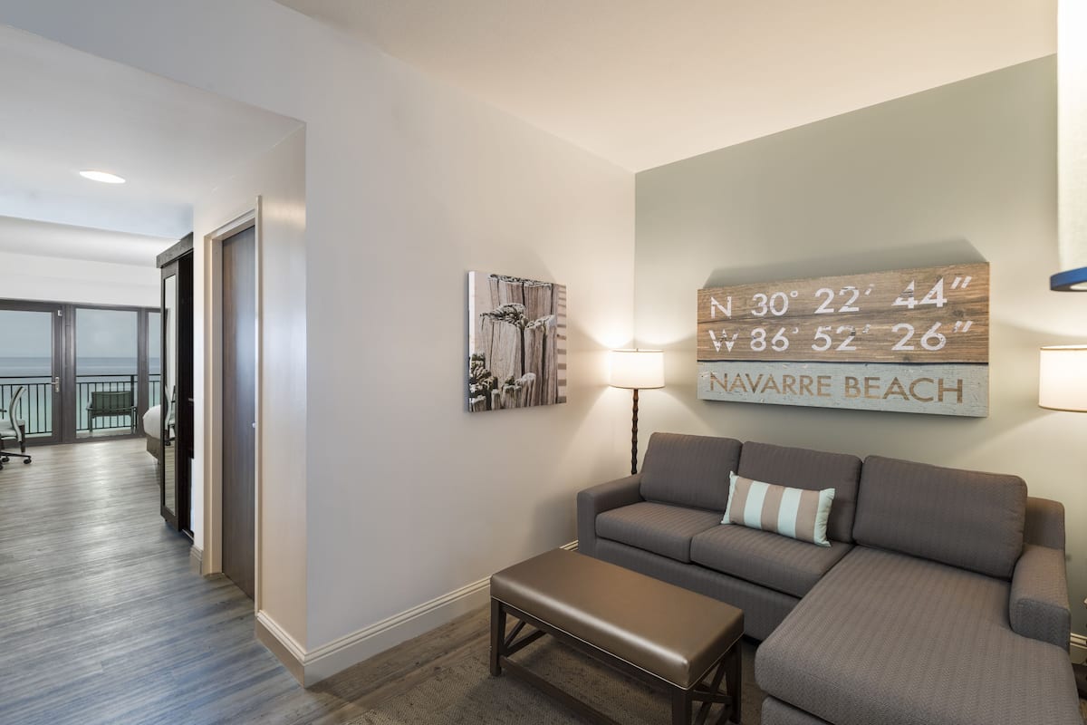A modern living room with a gray sofa, a bench, and a wall-mounted sign displaying coordinates.