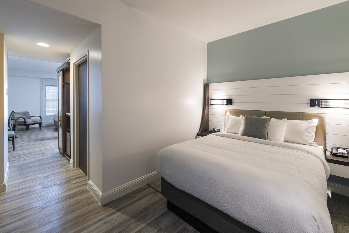 Une chambre d’hôtel moderne avec un grand lit, une table de chevet avec un téléphone et une vue sur le couloir.