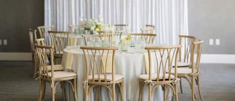 Un comedor con mesas redondas y sillas de madera, frente a un conjunto de persianas verticales.