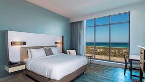 A modern hotel room with a large bed, a desk, and a view of the beach.