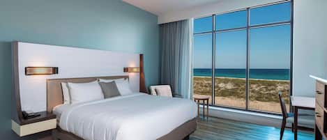 Une chambre d’hôtel moderne avec un grand lit, un bureau et une vue sur la plage.