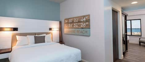 Ein Schlafzimmer mit einem großen Bett, einer Wandleuchte und Blick auf den Strand.