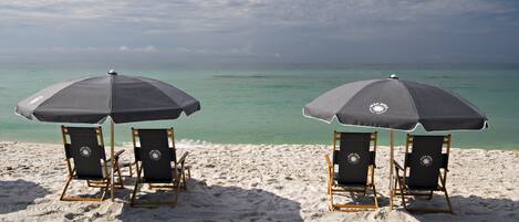 Deux chaises de plage avec des parasols, sur une plage de sable donnant sur l’océan.