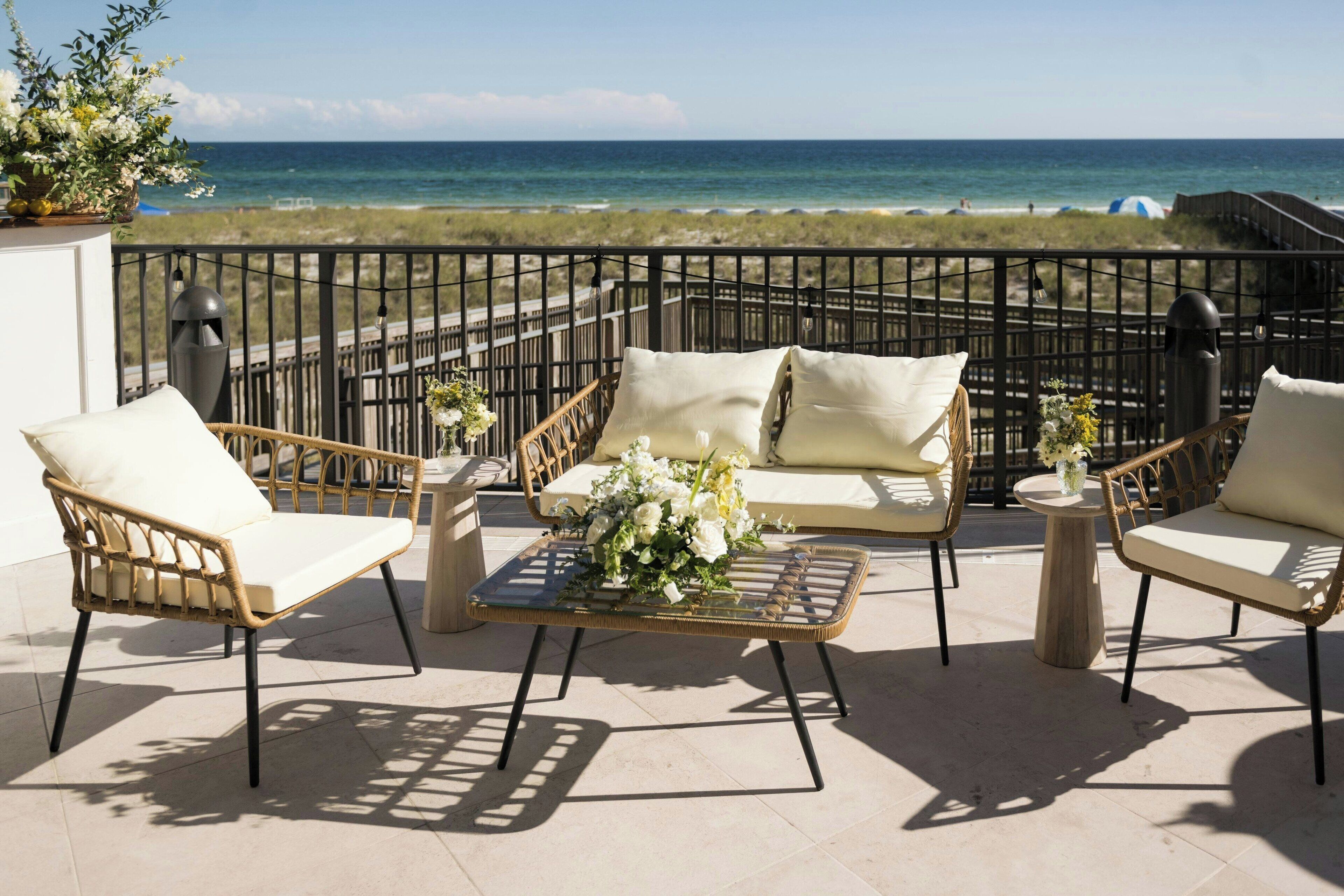 A balcony with wicker furniture, a glass table, and a flower arrangement.